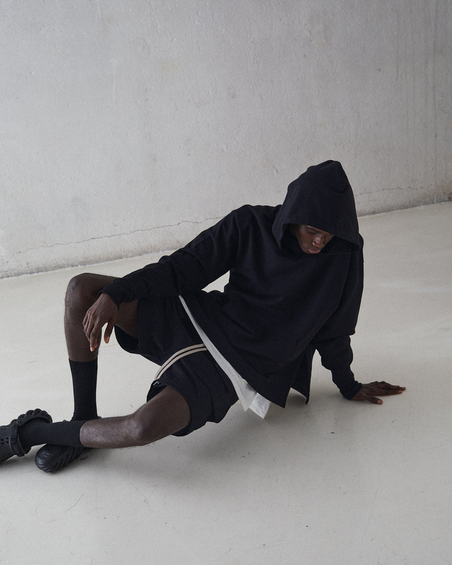 Male model laying on the floor wearing convertible pants as shorts and black hoodie