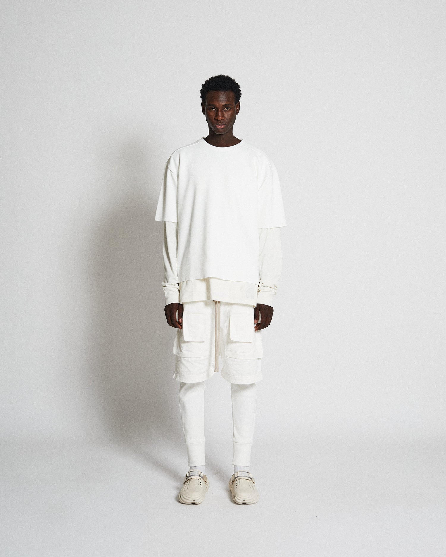Male model wearing all white convertible pants, long sleeve, leggings, and boxy t-shirt